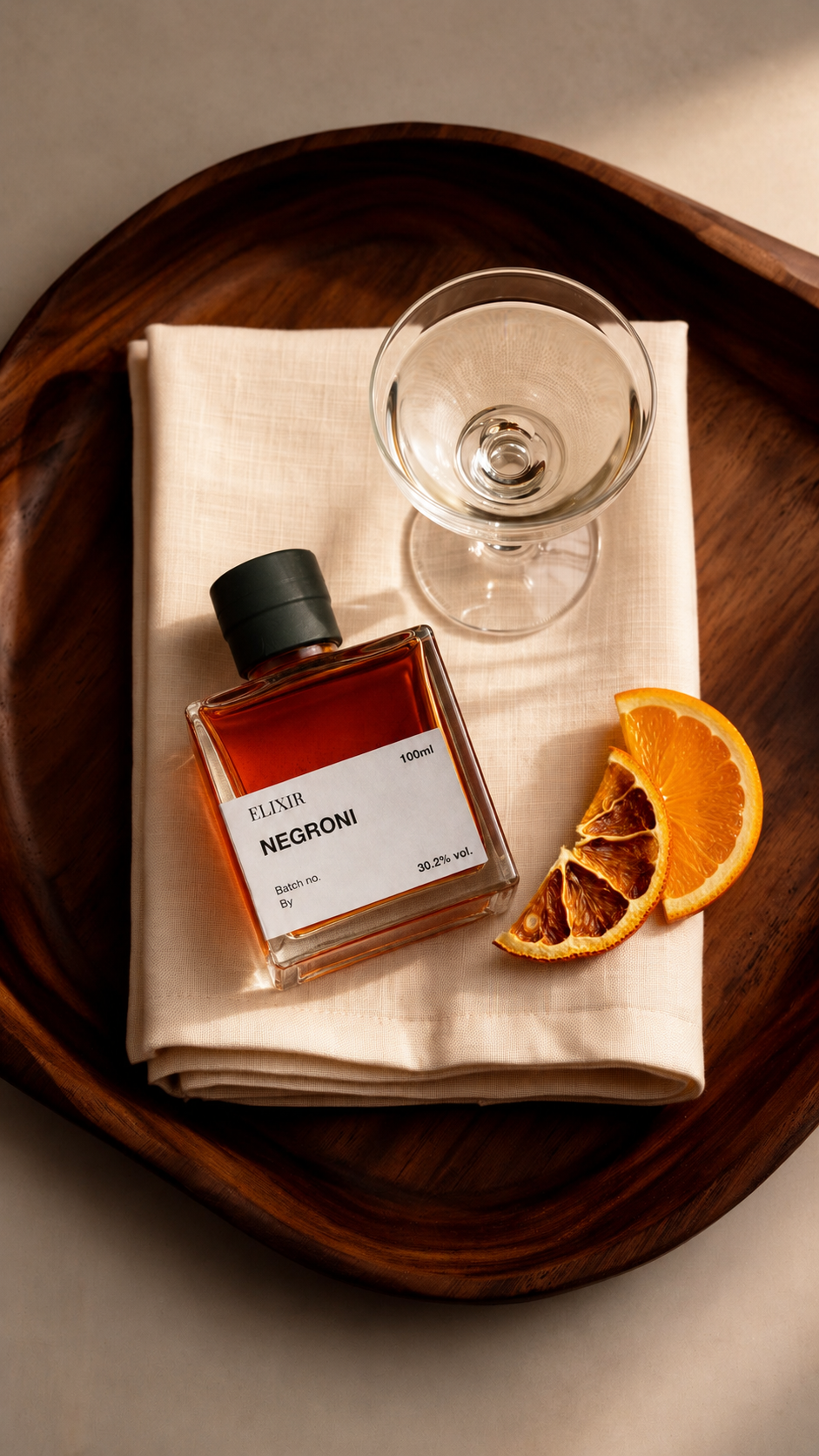Overhead arrangement of a square cocktail bottle, coupe, citrus and rosemary on a walnut tray